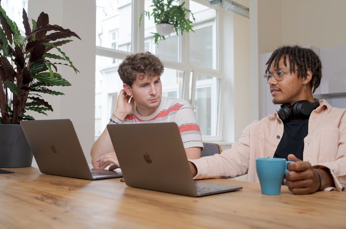 Two men collaborating at a table with laptops, focused on enhancing email engagement through content creation.