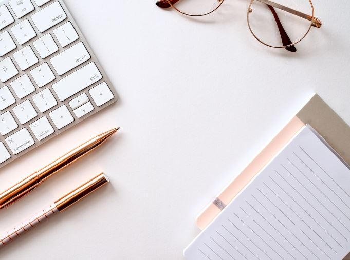 White desk with a keyboard, notebook, pen, and glasses neatly arranged