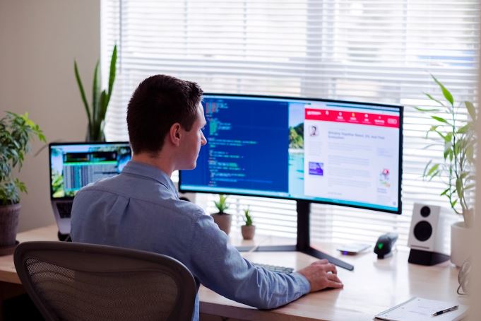 Man focused on work at a desk with two monitors displaying tasks and information.