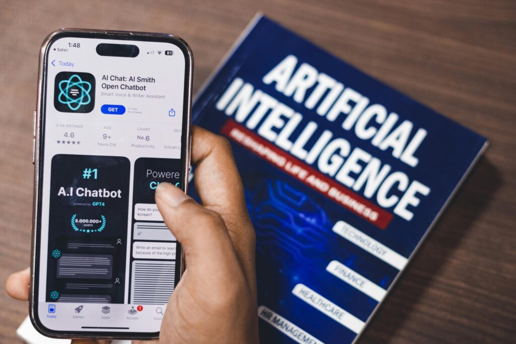 Person holding phone with AI chatbot app next to an Artificial Intelligence book.