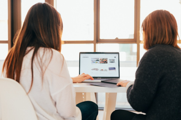 Two women collaborating on brand awareness strategies using a laptop in a bright office setting.