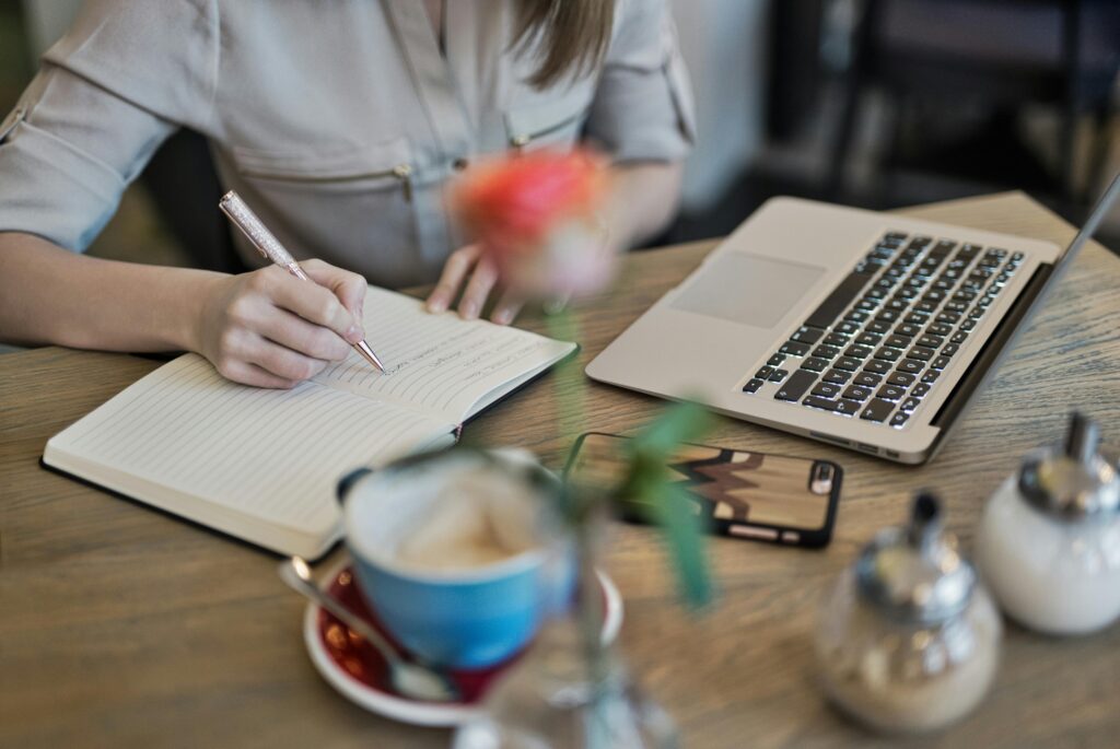 Person writing digital marketing strategy notes beside laptop