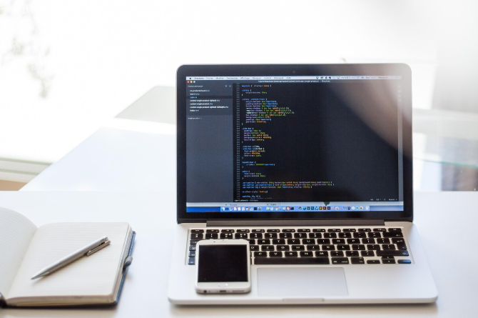 Laptop displaying code with smartphone and notebook, illustrating mobile SEO and page speed optimization.