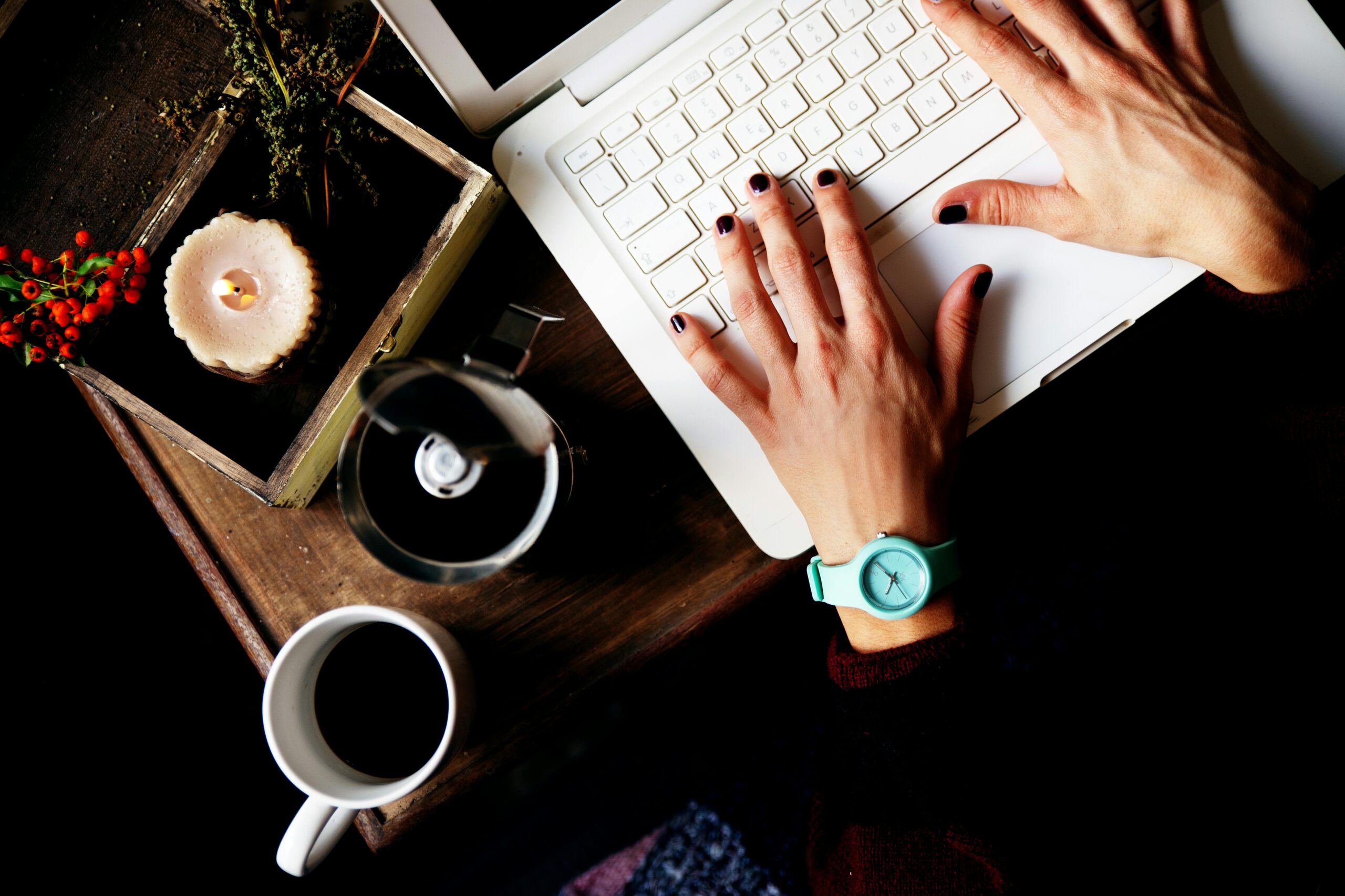 Person typing on laptop with coffee and candle nearby, symbolizing content creation for AI visibility.